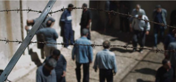 Group of people walking near barbed wire fence during night scene.
